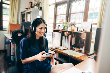 Young adult asian woman hand holding a joy controller wear headset and play game at home