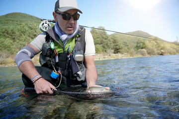 fly fisherman in summer catching a rainbow trout fishing in a mountain river