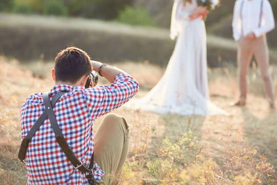professional photographer takes pictures of the bride and groom in nature on the sunset, wedding photographer in action