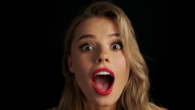 Young beautiful shocked amazing woman with red lipstick posing isolated over black background