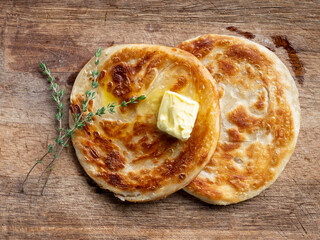 Rosy fritters with a slice of butter and herbs on a wooden background. View from above.