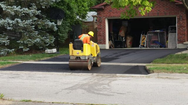 A Roller Is Being Used During An Asphalt Paving Job On A Residential Driveway, Ensuring Proper Compaction And Smoothness Of The Surface.