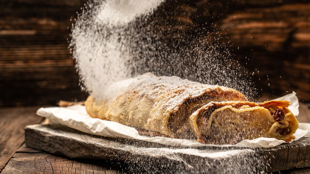 Apple strudel cake with cinnamon and raisins, sieve sprinkling sugar powder from above. austrian germany food