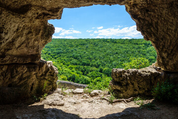 View from cave window onto endless forest near ancient city Chufut-Kale, Bakhchisaray, Crimea. Caves like this were used for different goals such as living, storing, even for religious. - obrazy, fototapety, plakaty