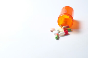 many colorful pills and capsules spilling form a container on white background 