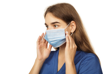 Beautiful young woman doctor surgeon putting on a protective disposable face mask isolated on white background. Virus protection concept. The modern viral threat of coronavirus