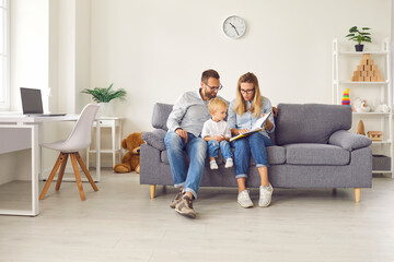 Mom shows pictures in a book to her little son, who is sitting with her and dad on the couch in the room.