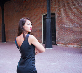 Beautiful girl with black hair. stands with his back, beautiful back and arms, looks up against the background of a brick wall