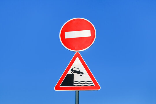Combination of international road signs 'No entrance (No entry)' & 'River bank (Quayside)' on clear blue sky background