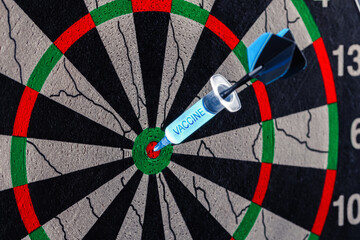 A disposable syringe in the form of a dart with the inscription Vaccine in the bull's eye of a dart board isolated on a white background. Coronavirus vaccine concept