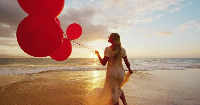 Happy young woman on the beach with red balloons at sunset