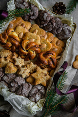 Gift box with different homemade cookies (gingerbread, almond, chocolate) and cinnamon buns decorated with fir tree branches and pine cones on wooden table.