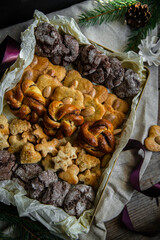 Gift box with different homemade cookies (gingerbread, almond, chocolate) and cinnamon buns decorated with fir tree branches and pine cones on wooden table.