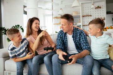 Husband and wife playing video games with joysticks in living room. Loving couple are playing video games with kids at home.