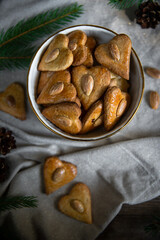 Bowl with heart-shaped gingerbread cookies with almond, espresso coffee, candle and fir branches on linen glittering fabric on wooden background,
