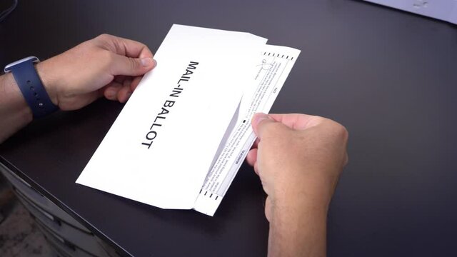 A man puts his mail-in ballot in the official envelope.  	
