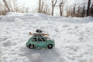 a small toy car is driving through the snow on a journey, the car is stuck in the snow, winter travel concept, yellow surfboard is lying on the roof of the car - Powered by Adobe