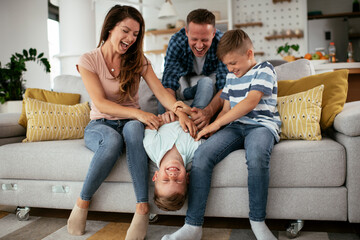 Young family enjoying at home. Mother and father tickling son.