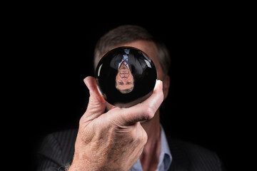 Senior caucasian hand holding glass sphere with upside down reflection of head. Concept for fear of...