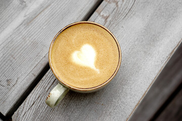 Cup of coffee on wood background. Latte art heart shape foam. Cappuccino cup top view. 