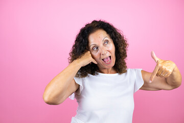 Middle age woman wearing casual white shirt standing over isolated pink background doing the “call me” gesture with her hands.