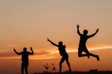 Silhouette of three Indian friends jumping with arms raised against the sky during the sunset	