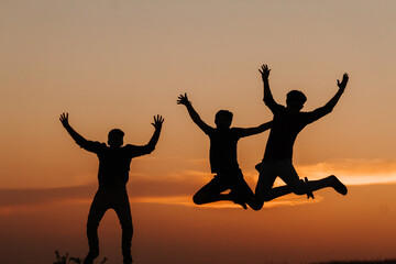 Silhouette of three Indian friends jumping with arms raised against the sky during the sunset	