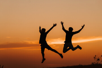 Fototapeta na wymiar Silhouette of two Indian friends jumping with arms raised against the sky during the sunset 
