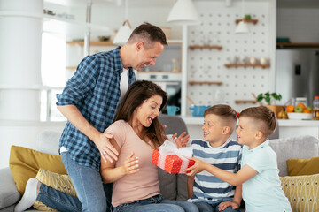 Two young sons are giving their mother a gift. Mother is suprised to receive a present from sons.