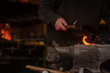 Close-up of the hands of a blacksmith forging a spiral from an iron bar with a hammer and anvil. Forging process with flying sparks. Work in the forge