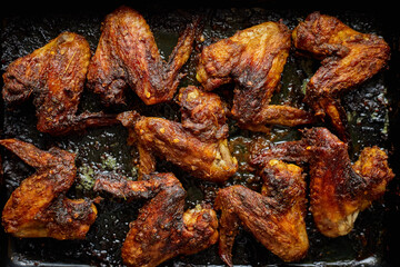 Grilled chicken wings in spices in black metal baking tray on stone table. Top view