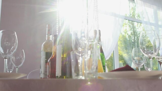 Beautiful table setting at a banquet, bottles with alcohol glasses stand on a decorated table against the background of the sun
