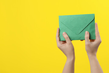 Woman holding green paper envelope on yellow background, closeup. Space for text