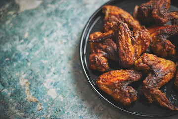 Grilled chicken wings on a black ceramic plate. Placed on a stone