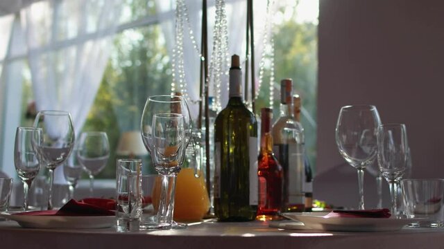 A beautiful room for a party, table setting, glasses and bottles of cognac, wine. Table decoration for the holiday, the sun in the window