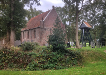 Fototapeta na wymiar Small Dutch church with graveyard at Nieuweschoot Heerenveen Friesland Netherlands. Tombstones. Bell chair.