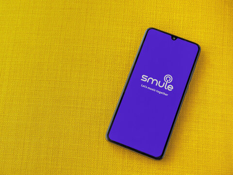 Lod, Israel - July 8, 2020: Smule app launch screen with logo on the display of a black mobile smartphone on a yellow fabric background. Top view flat lay with copy space.