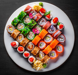 set of sushi roll with salmon, avocado, cream cheese, cucumber, rice, caviar, eel, tuna in plate on black wooden table