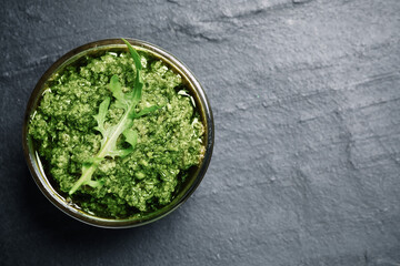 Bowl with tasty arugula pesto on black table, top view. Space for text