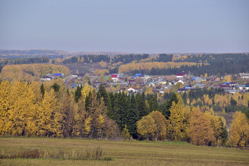 Fototapeta na wymiar The village among the Ural fields and forests in autumn decoration. In the foothills of the Western Urals, golden autumn.