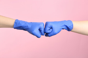 People in medical gloves doing fist bump on pink background, closeup of hands