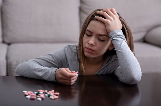 Hopeless young woman with depression planning to commit suicide by overdosing on meds at home