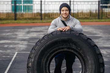 Fototapeta na wymiar Thirty-year-old strong athlete resting on a tire after training in the fresh air. Sports lifestyle.