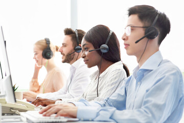Line of call centre representatives with headsets working on computers at open space office