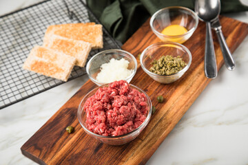 Gourmet Rindertatar Beef Tatar  aus Rindfleisch Filet fettarm  und roh, Kapern, Eigelb, Zwiebeln, Toast Brot auf Holzbrett und Marmor Hintergrund hell
