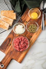 Gourmet Rindertatar Beef Tatar  aus Rindfleisch Filet fettarm  und roh, Kapern, Eigelb, Zwiebeln, Toast Brot auf Holzbrett und Marmor Hintergrund hell