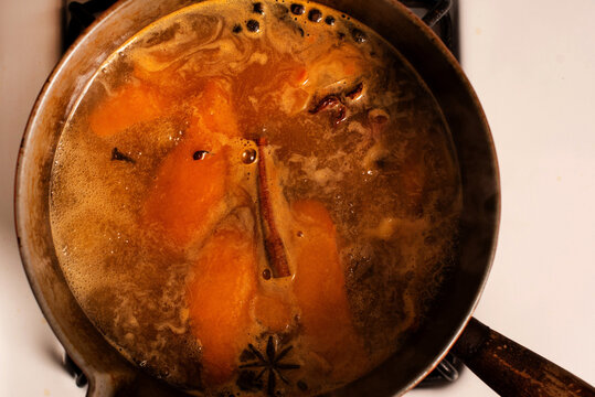 A sauce pan of mulled apple cider and orange cocktail simmers on the stovetop.