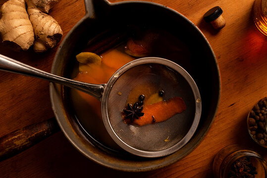 Strainer in a sauce pan of mulled apple cider and orange cocktail.