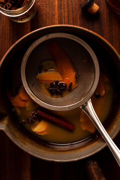 Strainer in a sauce pan of mulled apple cider and orange cocktail.