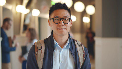 Portrait of cheerful asian male student with backpack posing indoors